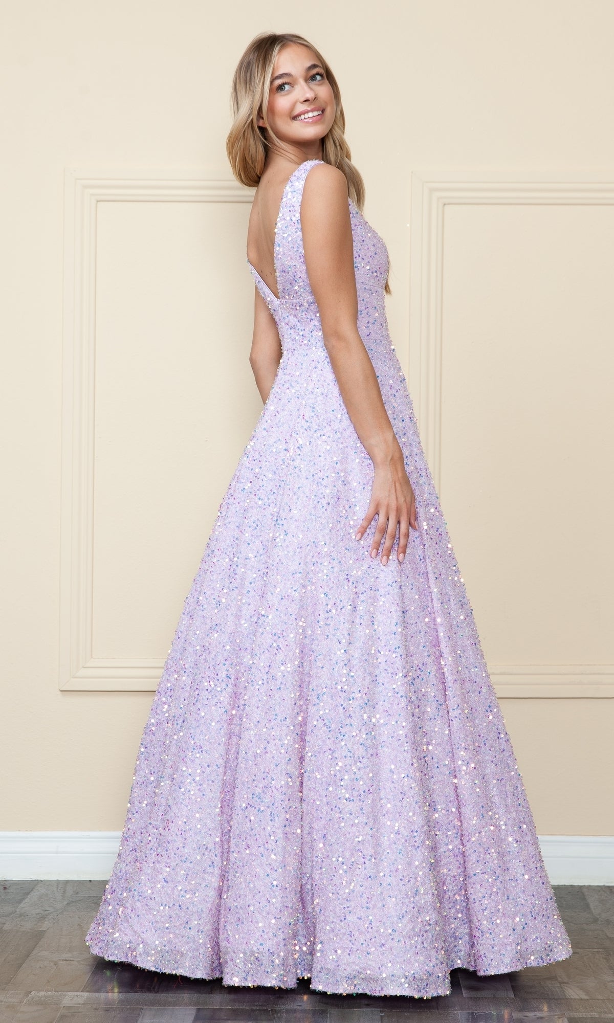 A woman stands indoors wearing the Long Black Sequin A-Line Prom Dress 9168, a floor-length sleeveless gown adorned with sparkling sequins, as she looks over her shoulder and smiles.
